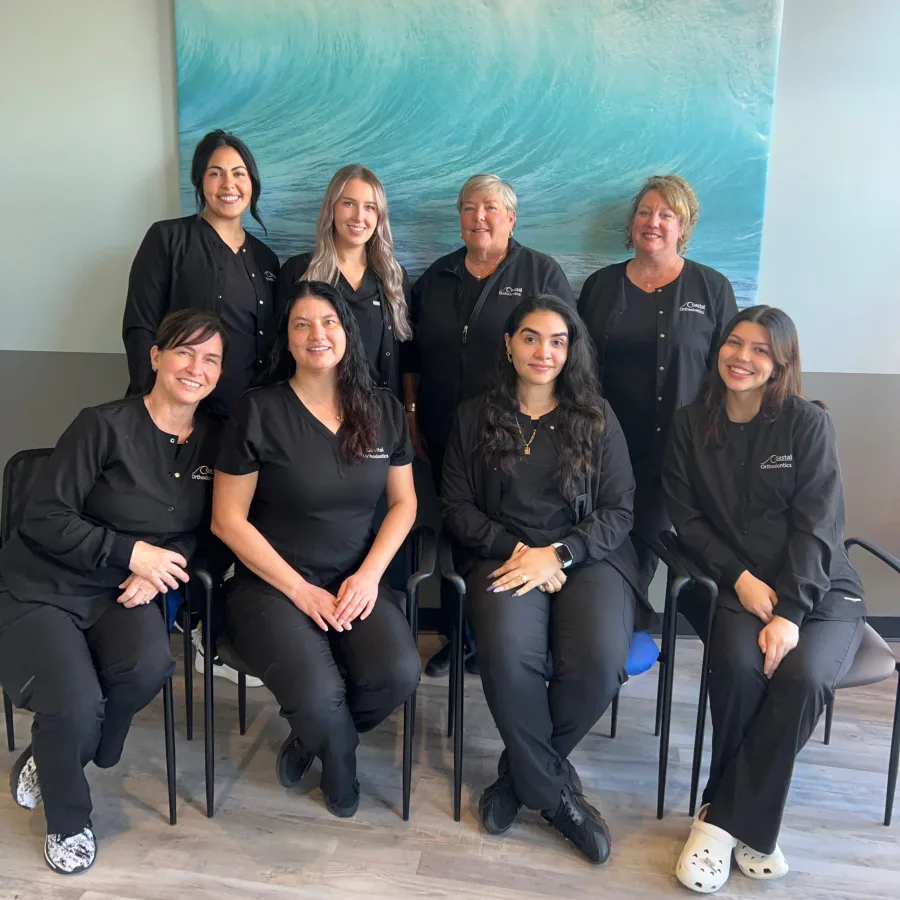 The Coastal Orthodontics team seated and standing in front of an ocean wave painting